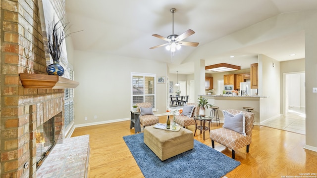 living room featuring ceiling fan, lofted ceiling, a brick fireplace, and light hardwood / wood-style flooring