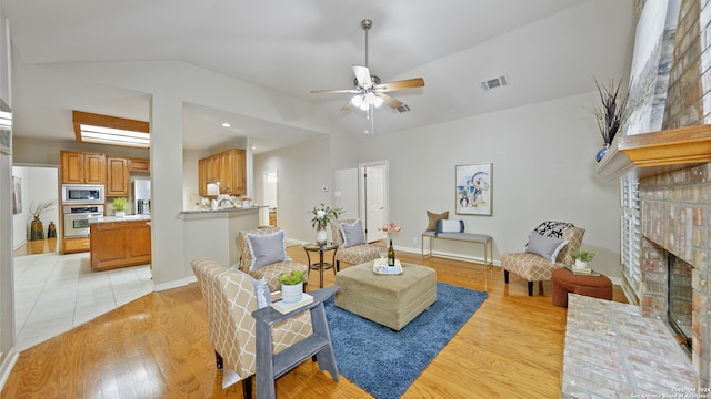 living room with a fireplace, ceiling fan, light hardwood / wood-style flooring, and vaulted ceiling