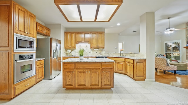 kitchen featuring kitchen peninsula, light stone counters, ceiling fan, and stainless steel appliances