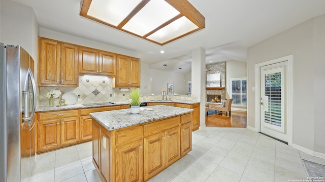 kitchen with black electric cooktop, light stone counters, a center island, stainless steel fridge, and decorative backsplash