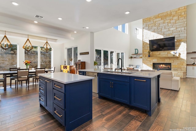 kitchen with blue cabinetry, a center island with sink, sink, and a stone fireplace