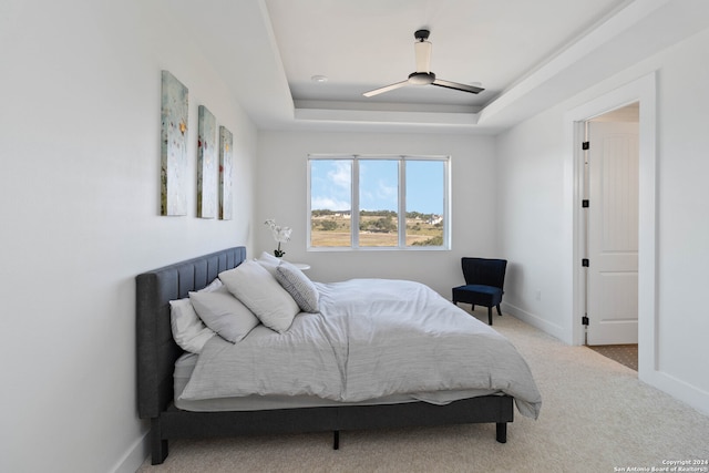 carpeted bedroom with ceiling fan and a raised ceiling