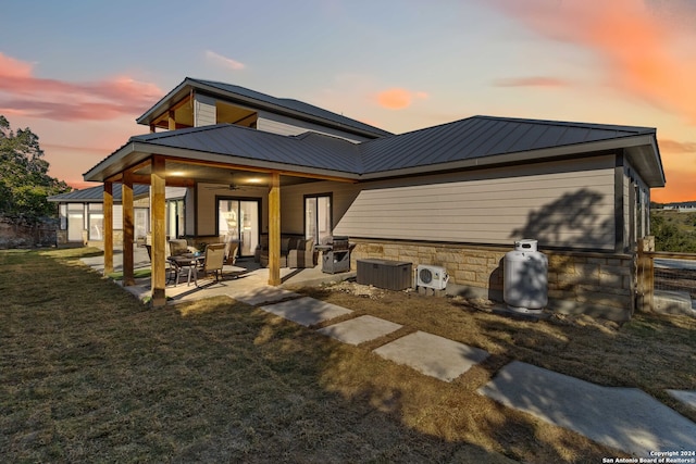 back house at dusk with ceiling fan, central AC, a yard, and a patio area