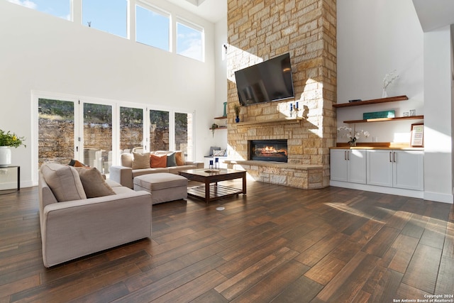 living room with a towering ceiling, dark hardwood / wood-style floors, and a stone fireplace