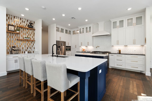 kitchen with stainless steel appliances, sink, custom exhaust hood, an island with sink, and dark hardwood / wood-style flooring