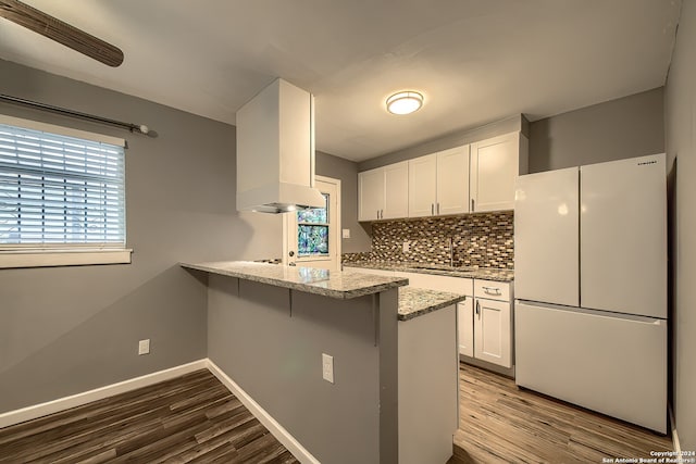 kitchen featuring white fridge, light stone countertops, hardwood / wood-style flooring, white cabinets, and kitchen peninsula