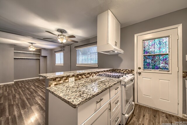 kitchen featuring dark wood-type flooring, white gas range oven, white cabinets, kitchen peninsula, and light stone countertops