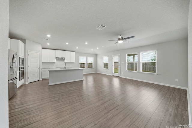 unfurnished living room featuring a textured ceiling, wood-type flooring, ceiling fan, and sink