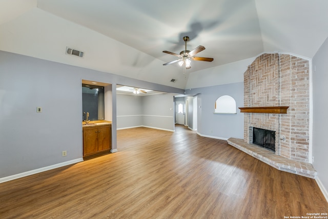 unfurnished living room with wood-type flooring, a stone fireplace, sink, lofted ceiling, and ceiling fan