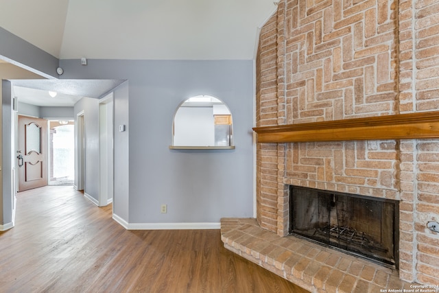 unfurnished living room featuring a brick fireplace, wood-type flooring, and lofted ceiling