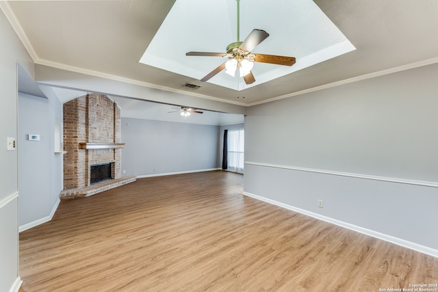 unfurnished living room with light hardwood / wood-style floors, ceiling fan, a fireplace, a raised ceiling, and crown molding