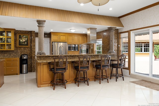 kitchen featuring a kitchen bar, a healthy amount of sunlight, ornate columns, and appliances with stainless steel finishes