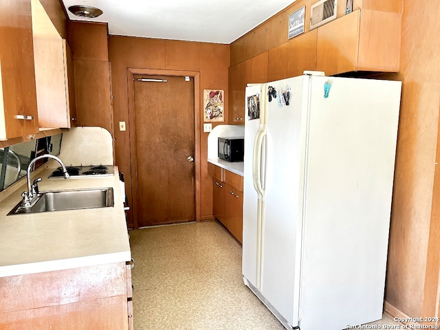 kitchen with wood walls, sink, and white refrigerator with ice dispenser