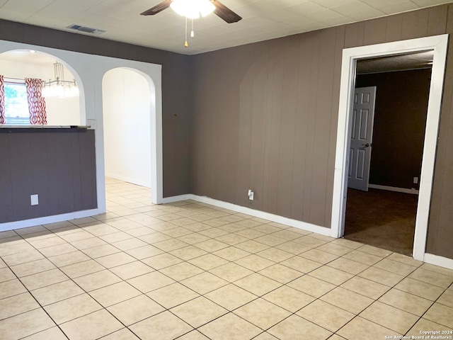 tiled empty room featuring wood walls and ceiling fan with notable chandelier