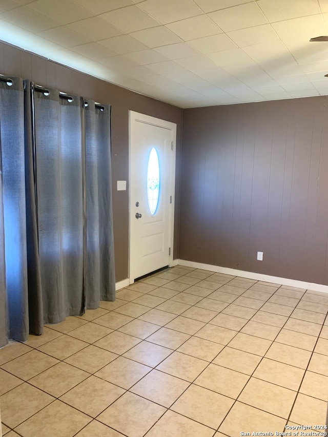 foyer entrance with ceiling fan, light tile patterned floors, and wood walls