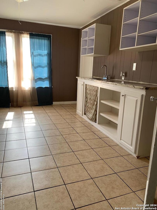 kitchen with white cabinets, light tile patterned floors, wooden walls, and sink