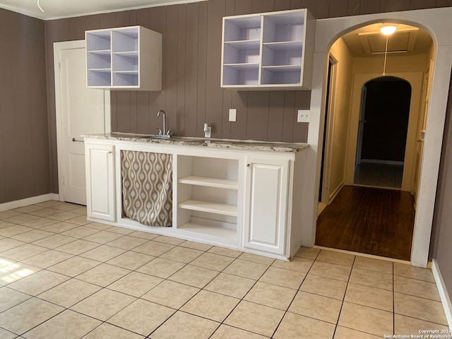 bar with wood walls, white cabinets, sink, and light wood-type flooring