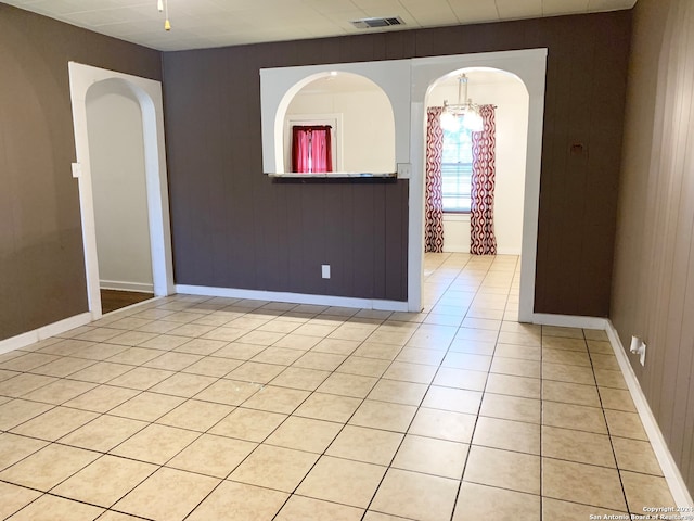 empty room with wood walls, light tile patterned floors, and a notable chandelier