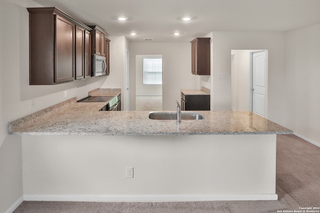 kitchen with kitchen peninsula, light carpet, black stove, and sink