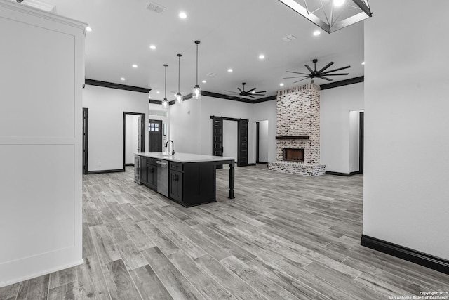 kitchen featuring pendant lighting, ornamental molding, a kitchen island with sink, ceiling fan, and a brick fireplace