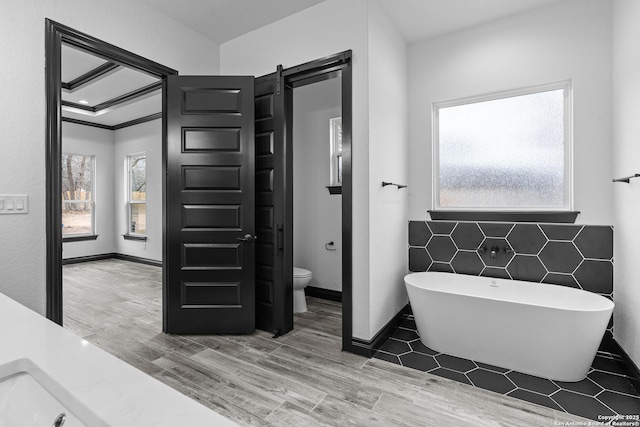 bathroom with hardwood / wood-style flooring, toilet, a wealth of natural light, and a tub to relax in