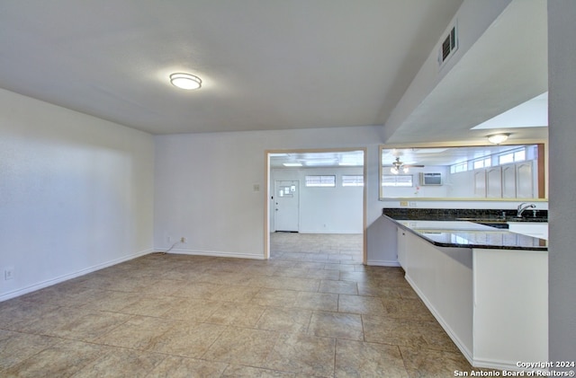 kitchen with kitchen peninsula, ceiling fan, sink, and white cabinets