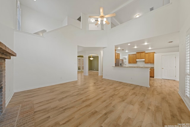 unfurnished living room with a fireplace, light hardwood / wood-style floors, high vaulted ceiling, and ceiling fan