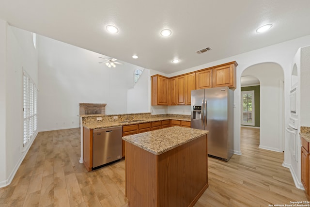 kitchen with a center island, light stone counters, light hardwood / wood-style flooring, kitchen peninsula, and appliances with stainless steel finishes