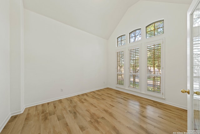 empty room featuring high vaulted ceiling, a healthy amount of sunlight, and light hardwood / wood-style floors