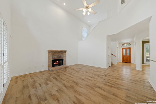 unfurnished living room featuring a high ceiling, a fireplace, ceiling fan, and light hardwood / wood-style flooring