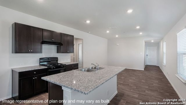 kitchen featuring black gas stove, sink, a center island with sink, dark wood-type flooring, and light stone countertops