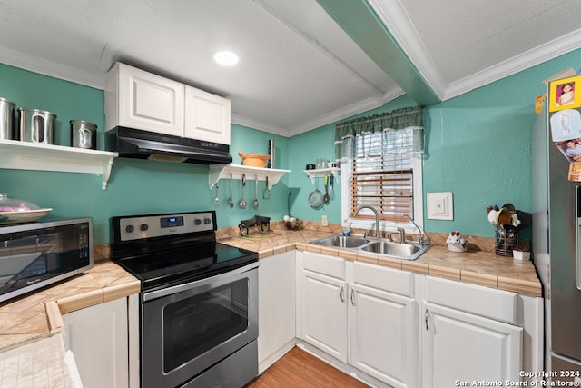 kitchen with sink, tile counters, appliances with stainless steel finishes, white cabinets, and ornamental molding