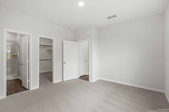 unfurnished bedroom with a closet, ensuite bath, a walk in closet, and dark colored carpet