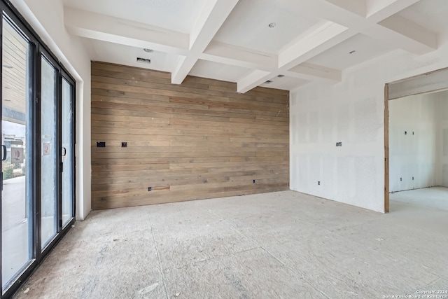 empty room featuring coffered ceiling, beam ceiling, and wood walls