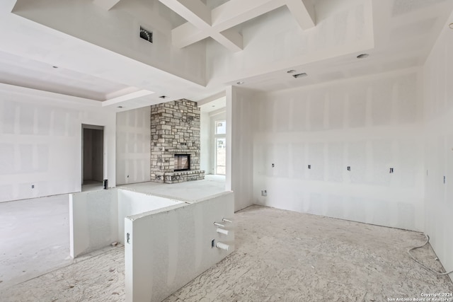 unfurnished living room with a stone fireplace, beamed ceiling, and coffered ceiling