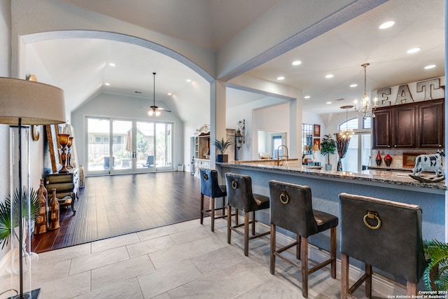 kitchen featuring dark brown cabinetry, light hardwood / wood-style flooring, decorative light fixtures, vaulted ceiling, and stone countertops