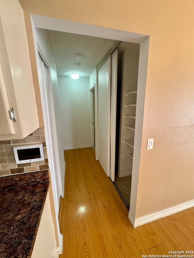 hall with a textured ceiling and light wood-type flooring