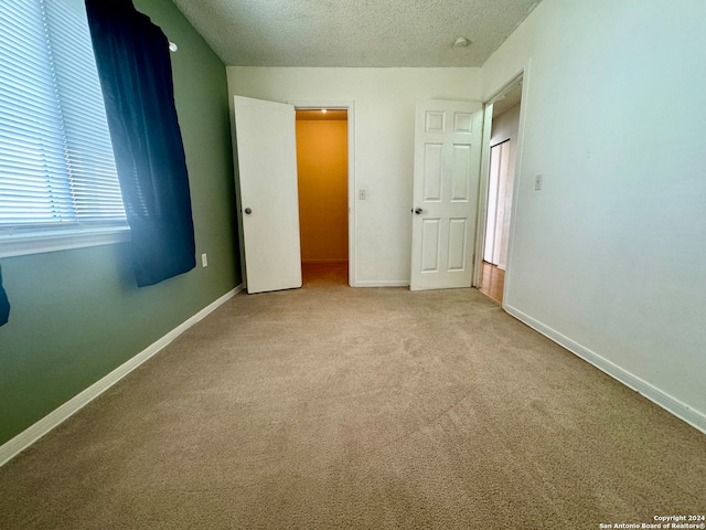 unfurnished bedroom featuring multiple windows, light colored carpet, and a textured ceiling