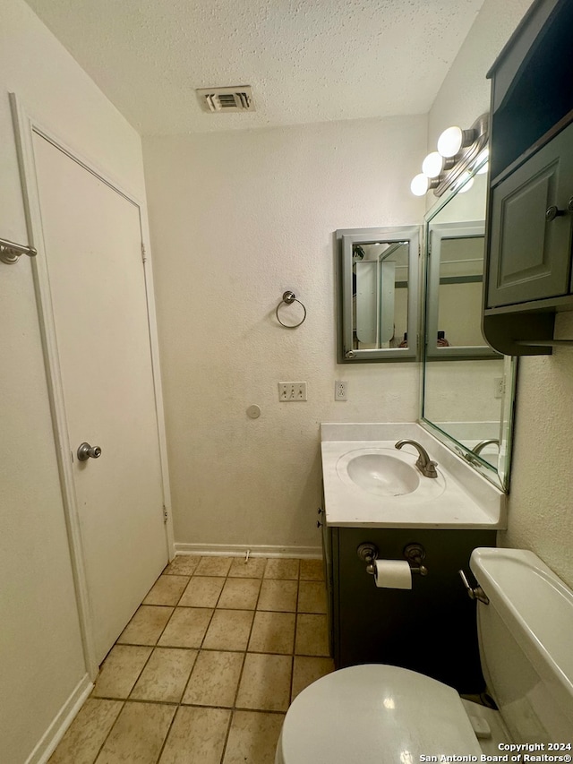 bathroom featuring vanity, toilet, tile patterned floors, and a textured ceiling