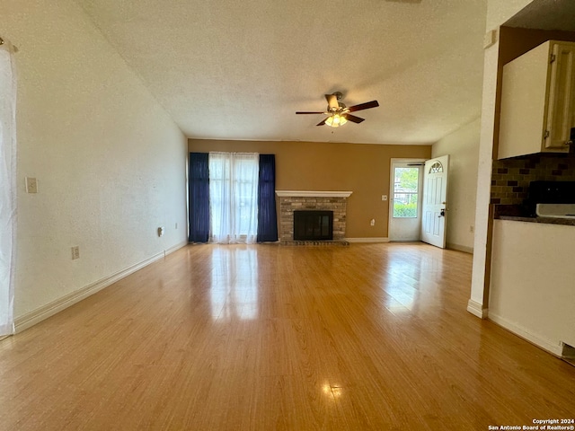 unfurnished living room with a fireplace, ceiling fan, light hardwood / wood-style flooring, and a textured ceiling