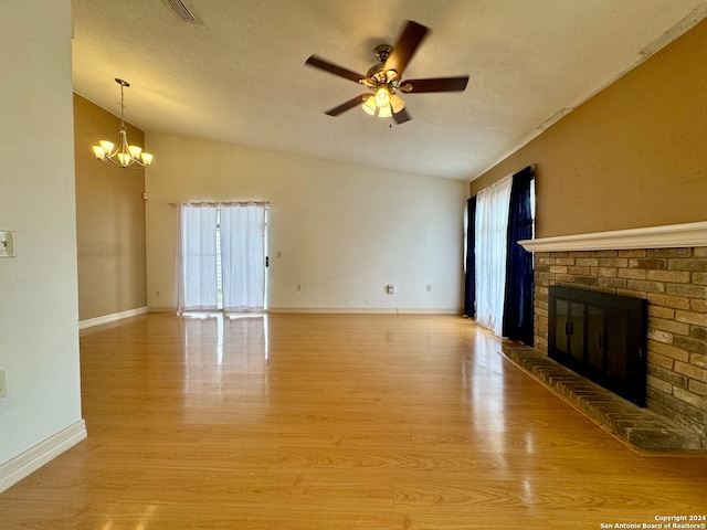 unfurnished living room featuring vaulted ceiling, a brick fireplace, light wood-type flooring, and a textured ceiling