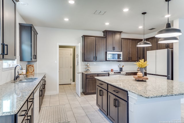 kitchen featuring appliances with stainless steel finishes, a center island, light stone countertops, pendant lighting, and sink