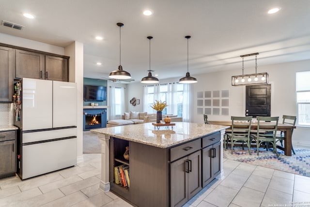 kitchen featuring white fridge, a center island, light stone countertops, pendant lighting, and dark brown cabinetry