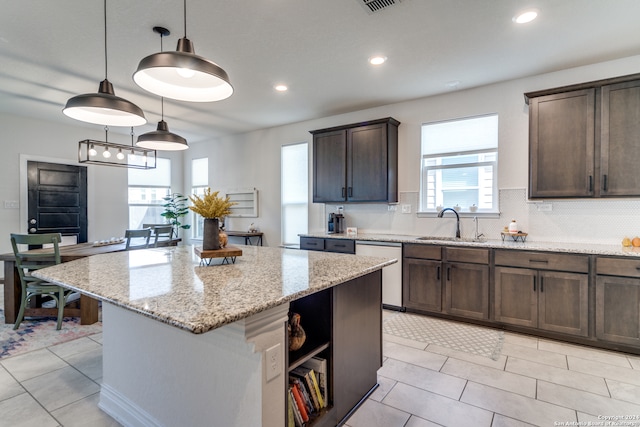 kitchen with decorative light fixtures, light stone counters, stainless steel dishwasher, dark brown cabinets, and a kitchen island