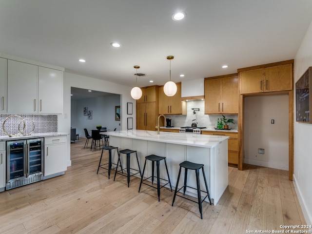 kitchen featuring white cabinetry, wine cooler, a center island with sink, hanging light fixtures, and light wood-type flooring