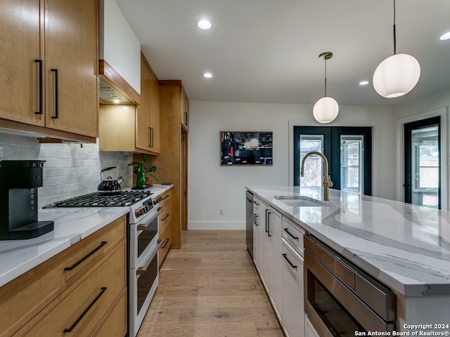 kitchen featuring light stone countertops, sink, hanging light fixtures, stainless steel appliances, and light hardwood / wood-style floors