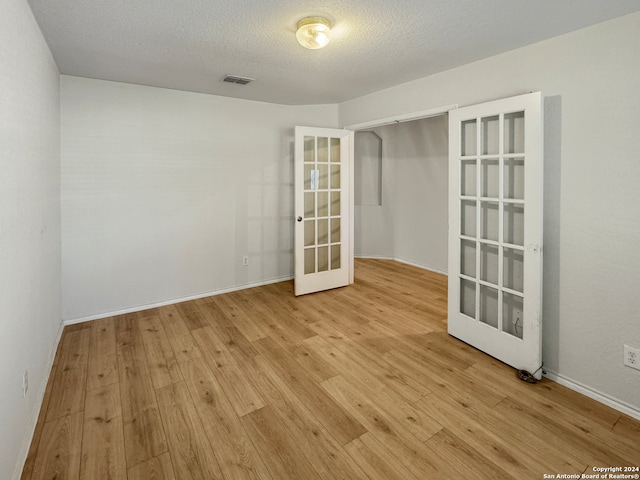 unfurnished room featuring light hardwood / wood-style flooring, a textured ceiling, and french doors