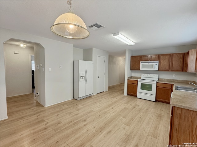 kitchen featuring decorative light fixtures, white appliances, sink, and light wood-type flooring