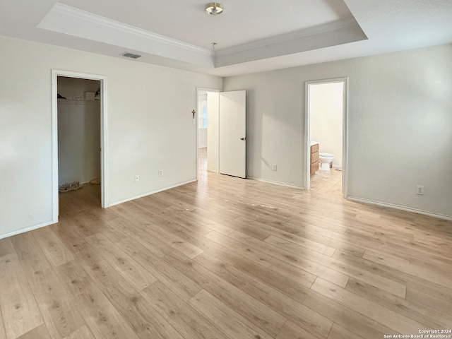 unfurnished bedroom with a raised ceiling, light wood-type flooring, and a spacious closet