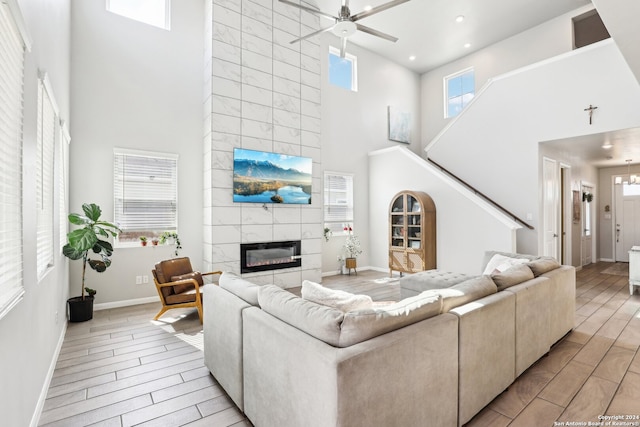 living room featuring a tile fireplace, a healthy amount of sunlight, a high ceiling, and light wood-type flooring